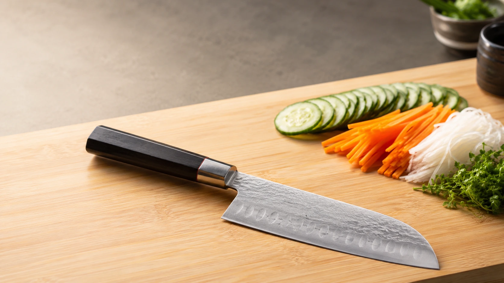Un superbe couteau de cuisine japonais de style Santoku posé de biais sur une grande planche à découper en bois clair. La lame en acier présente une finition martelée sur le dessus et une série d'alvéoles le long du tranchant. Le manche octogonal est en bois sombre mat. À côté, des légumes fraîchement préparés sont soigneusement alignés comme des rondelles de concombre, des bâtonnets de carotte en julienne, du radis blanc râpé et une touche de verdure fine.