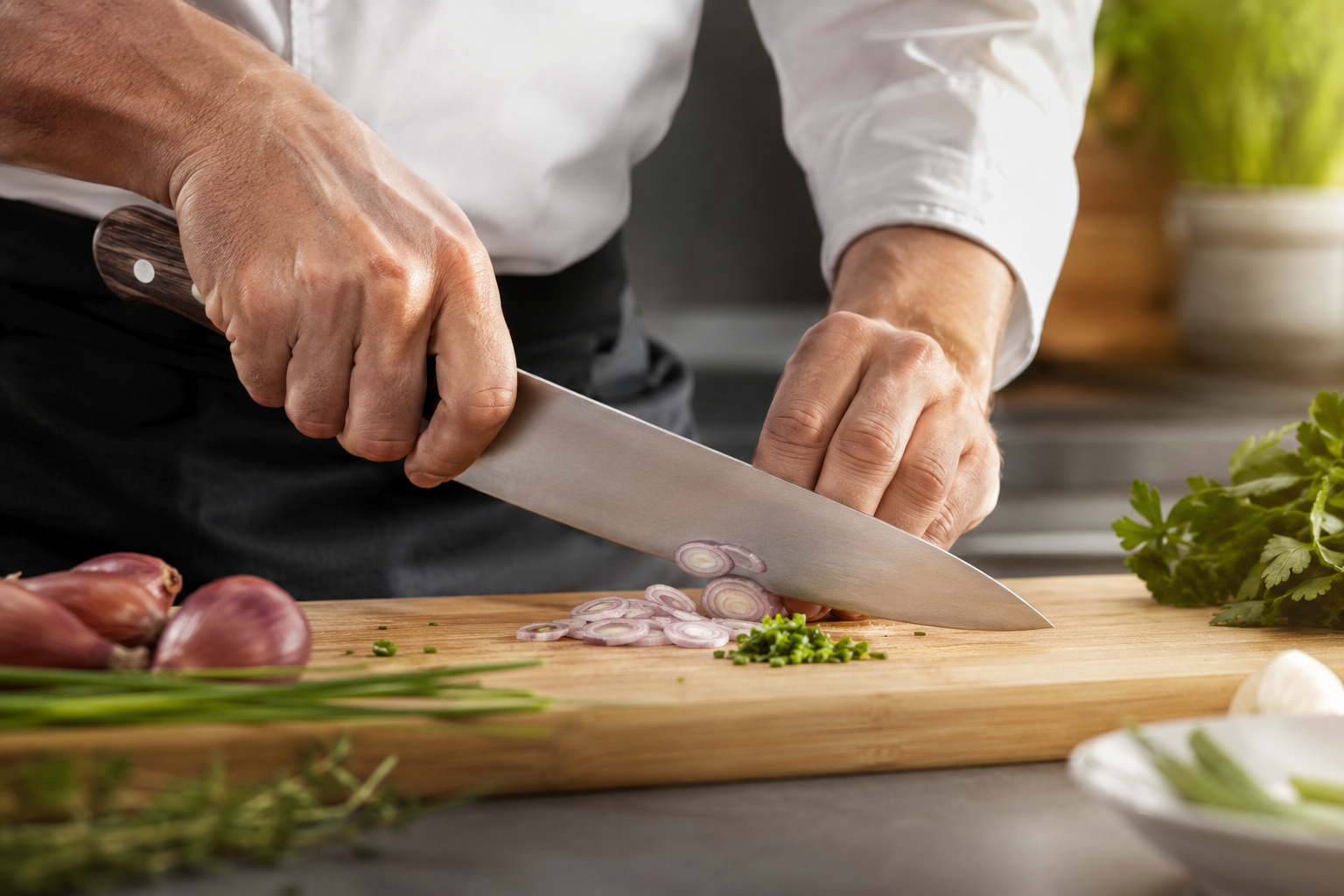 Chef cuisinier utilisant un grand couteau de cuisine français traditionnel à manche en bois pour émincer des échalotes sur une planche.
